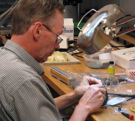 Roger Macauley soldering a DIN plug to a cab cable on the workbench at APN